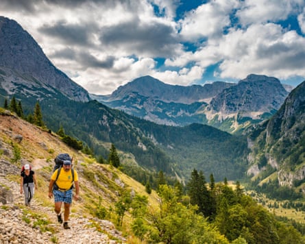 Hikers walk along a rocky trail with mountain peaks in the background