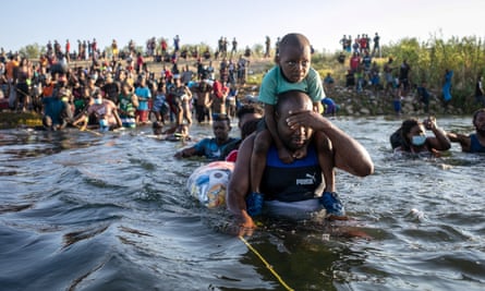 child rides on man's shoulders as man wades through water and covers his eyes