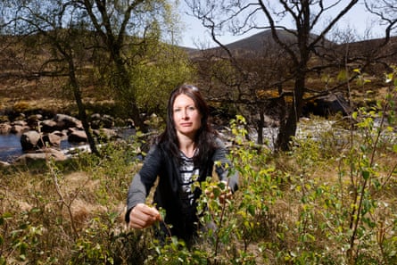 A woman standing among tree saplings on a riverbank