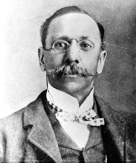 A Black man with a mustache, wearing thin-rimmed glasses and a bowtie