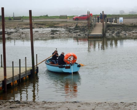 Someone rowing a small blue boat between two piers on a river on a misty day