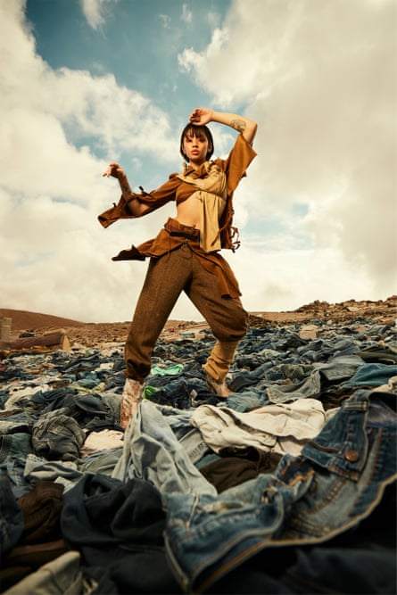 A model wearing brown trousers and a crop top poses against the desert sky