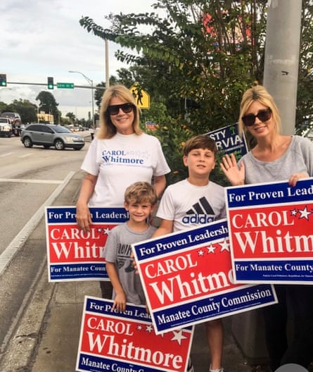 Two white women with blond hair and two grade school-age boys with brown hair, holding red, white and blue signs that says ‘For preoven leadership/Carol Whitman/Manatee County Commission’.