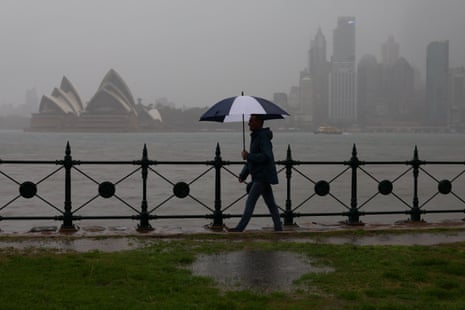 A person carrying an umbrella walks along the waterfront past Sydney Opera House in Sydney.