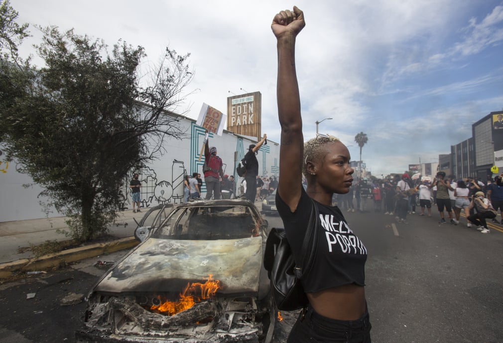 Los Angeles - Una ragazza alza il pugno davanti a un veicolo della polizia in fiamme (Fonte: Guardian; Photograph: Ringo H W Chiu/AP).