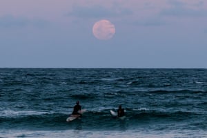 Surfers gaze at the full moon at Manly beach in Sydney, Australia