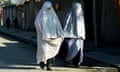 Two women wearing white burqas walk along a street