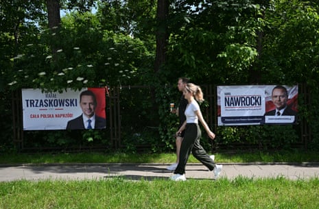 A woman and a man walk past election banners depicting presidential candidates Rafał Trzaskowski and Karol Nawrocki in Warsaw, Poland.