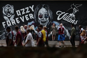 People walk past or pose next to a black-and-white mural depicting Ozzy Osbourne, with the words ‘Ozzy for ever’