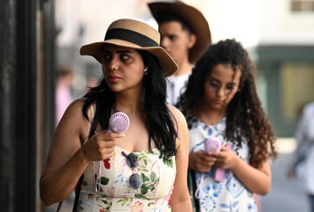 Two women and a man walk using handheld fans