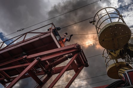 Picture from below, a man stands on a metal platform while repairing overhead lines