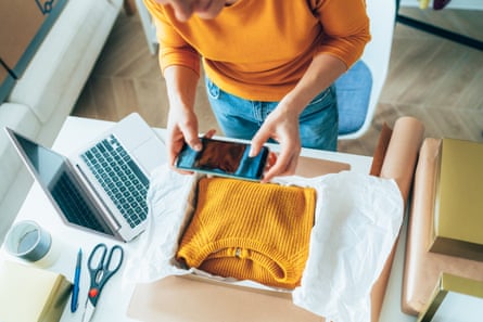 Young woman photographing a parcel wth a yellow jumper inside, by a laptop