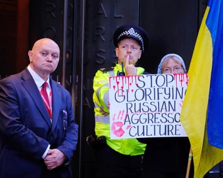 A protester holds a sign outside the Royal Opera House in London next to a police officer and security guard