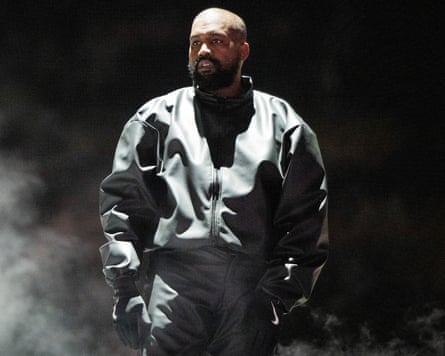 Kanye West on stage dressed in a black jacket, trousers and and black gloves