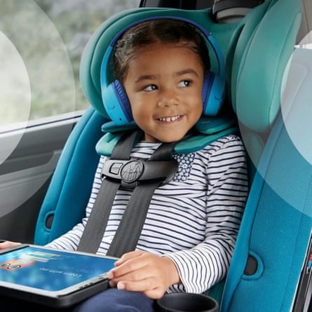 A contented child in the backseat of a car, wearing headphones and watching a programme on a tablet device.