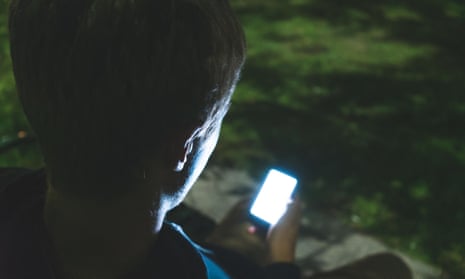 Depressed teenager on his mobile while sitting on a park bench at night.