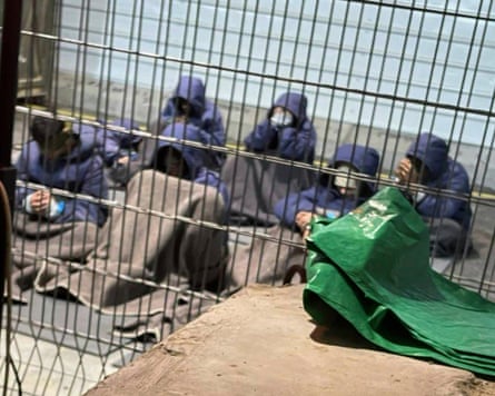 Prisoners with their hands and legs restrained in yard behind a wire fence