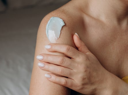 A close up of a woman applying lotion to her shoulder