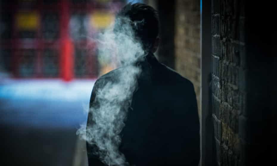 Man smoking in a dark alleyway.