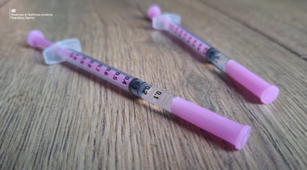 Two pink plastic syringes lie on a wooden surface