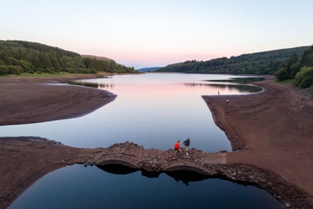 Two people walk across the exposed bridge within the dried-up reservoir