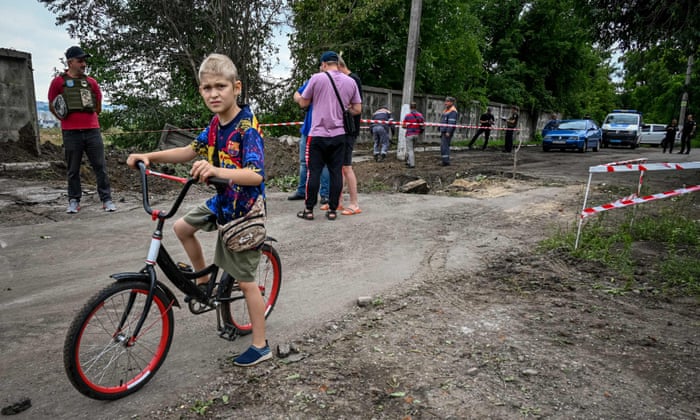 A boy pushes his bicycle while communal worker inspect a crater following a strike on the second largest Ukrainian city of Kharkiv on Wednesday.