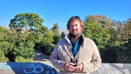 O’Donoghue looks at camera holding binoculars with trees in parkland behind