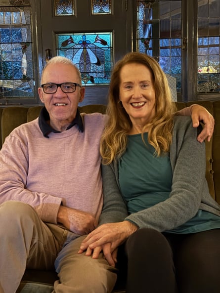 Steve and Martha, now in their 60s, sitting on a couch inside a house