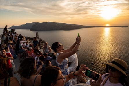 Tourists taking pictures and selfies during sunset in Santorini.