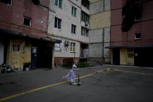 A girl rides a scooter near buildings destroyed during the Russiam attacks in Irpin