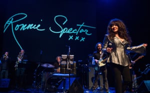 A woman performs on stage. Behind her, her signature is projected onto a screen