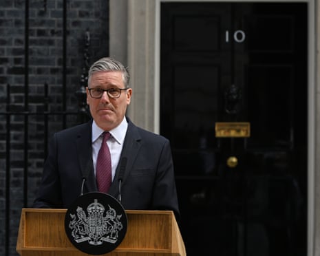 Starmer in suit jacket and tie behind lectern outside door of No10 looking pensive