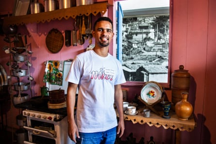 A young man stands in a replica kitchen done up in an older style with a monochrome photo behind the window to mimic the former view