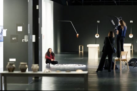 Paucar sits behind his work in a darkened studio; a line of earthenware pots is in the foreground, a woollen spiral on the floor, and illuminated installations in the background. Two women are taking his photograph as he sits on the floor.