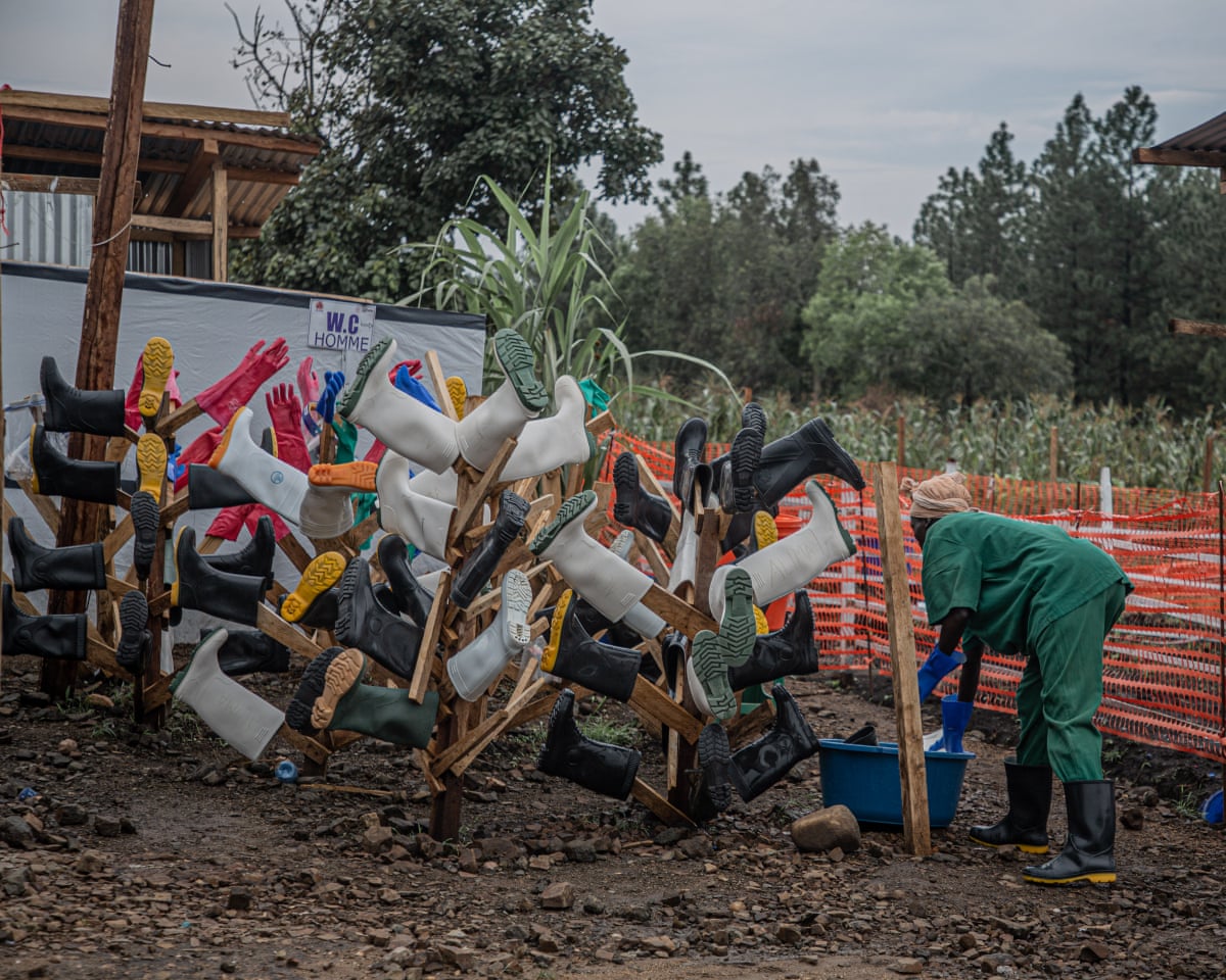 A woman washes a boot in a large bowl while others hang drying on tree-like wooden frames