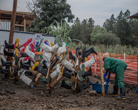 A woman washes a boot in a large bowl while others hang drying on tree-like wooden frames