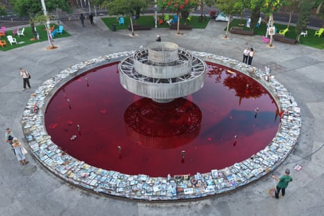 People look at the fountain filled with red-dyed water, with images of victims placed around it.