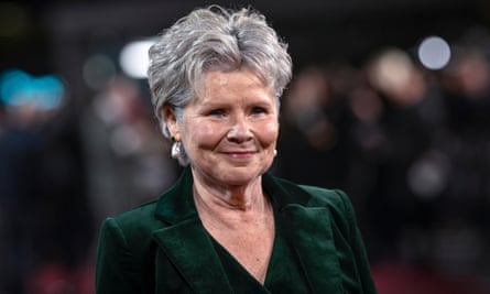 Imelda Staunton: she is seen against a dark background and wears a dark green velvet jacket; she has short grey hair and is wearing makeup and large dangling pearly earrings to attend an event at the Royal Festival Hall. 