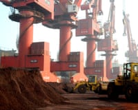 Yellow diggers work by huge heaps of reddish-brown soil and red cranes.
