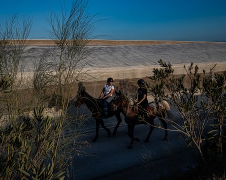 Karina and Alba ride their horses past plastic roofs