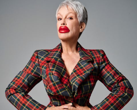 Portrait of Jamie Lee Curtis in a tartan jacket with her hands on her hips and sporting a huge pair of plastic red lips