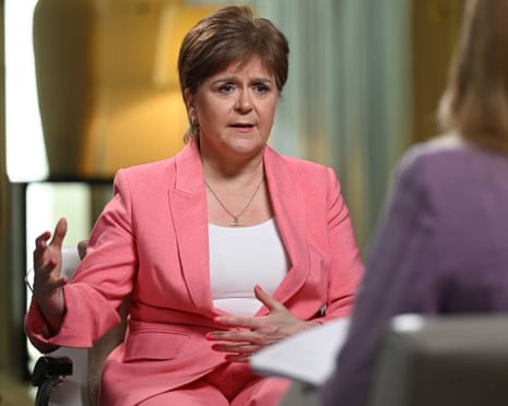 Sturgeon, in a pink suit, gestures while speaking during TV interview