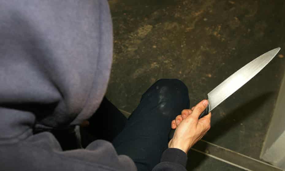 Man in a hoodie holding a knife.