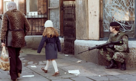 A woman and child walk past a British soldier on patrol in the New Lodge district of Belfast in 1978.