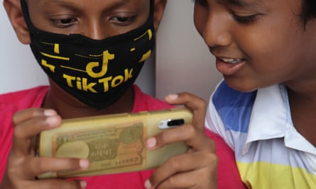 A boy wearing a face mask with the TikTok logo uses a mobile phone outside the downed shutters of a shop in Mumbai, India.