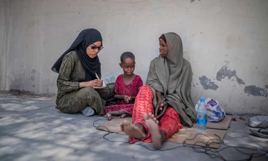 A reporter interviews a mother and her child sitting on a piece of cardboard on the street