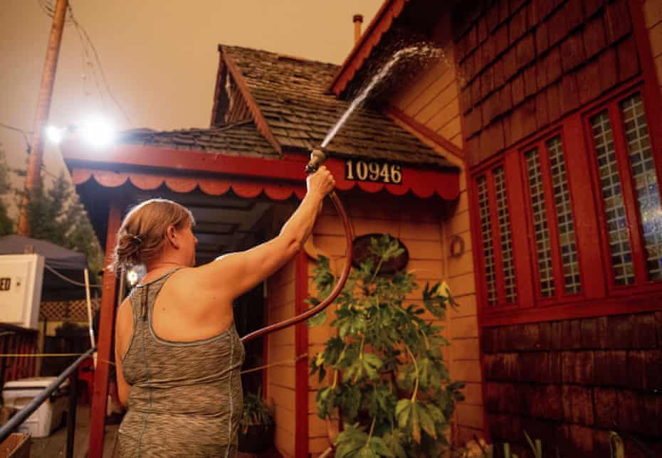 Jennifer Whitmore sprays her home with water as the Caldor fire burns near White Hall, California, on 17 August.