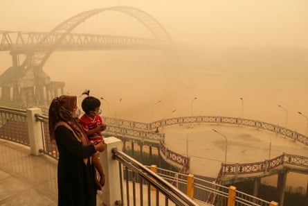 The pair stand amid thick haze as they look over a body of water.