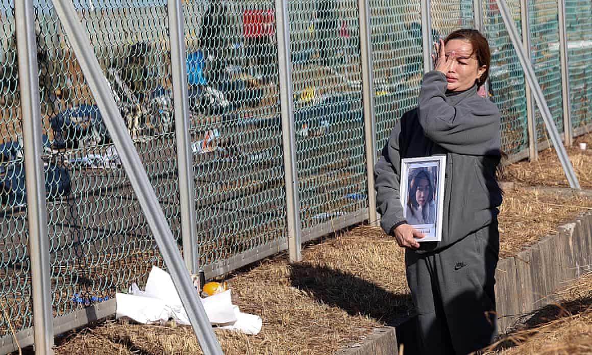 A woman holding a photo of a loved one cries while standing at a wire fence