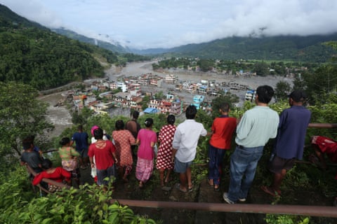 Group of villagers standing on a hillside, looking down at a town devastated by a severe flood in Nuwakot, Nepal